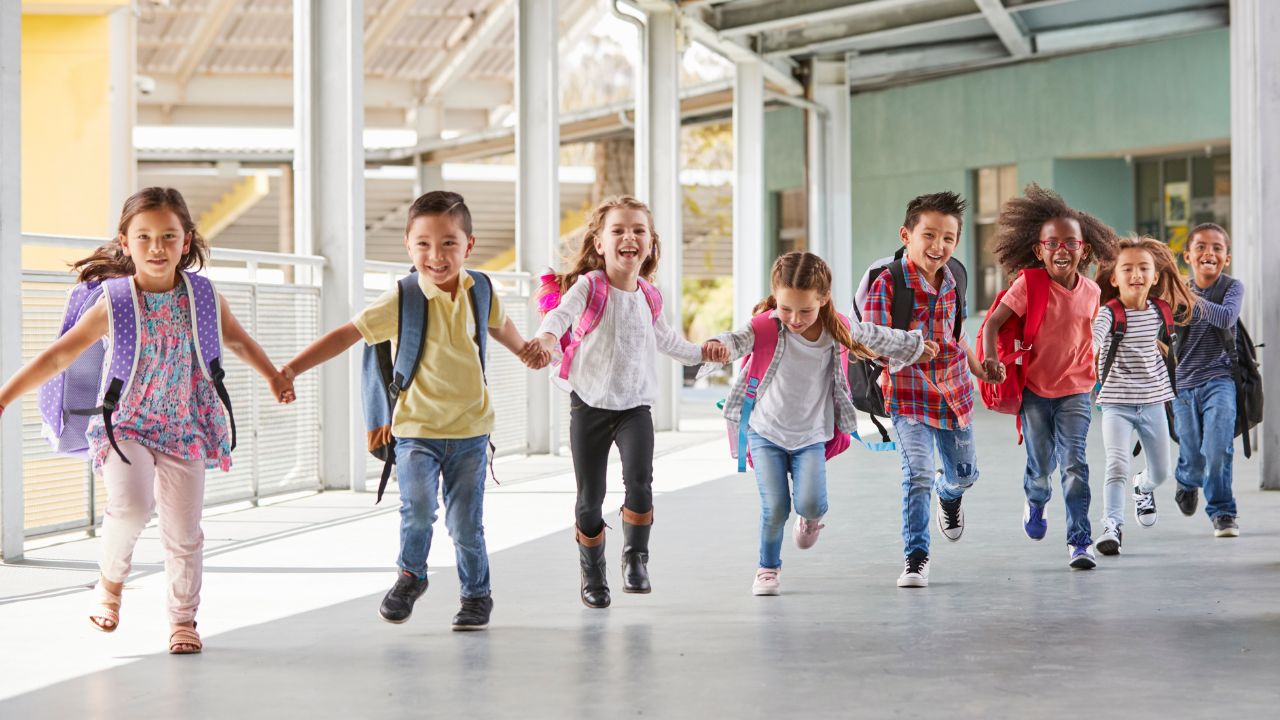 Primary school kids run holding hands in corridor