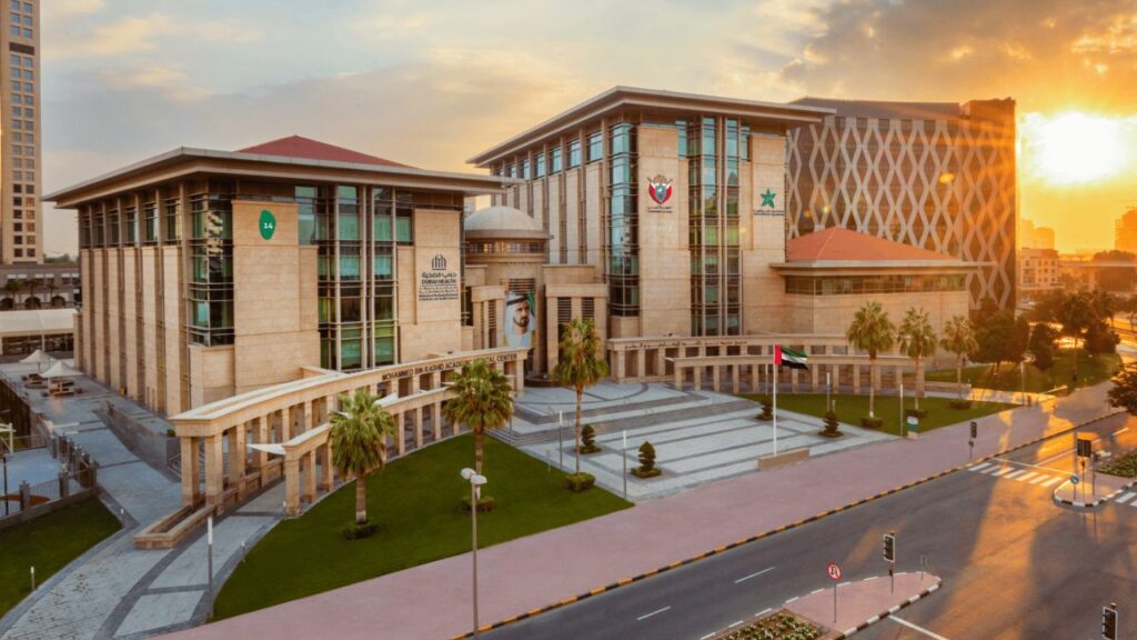 Modern university building at sunset with palm trees and cityscape.