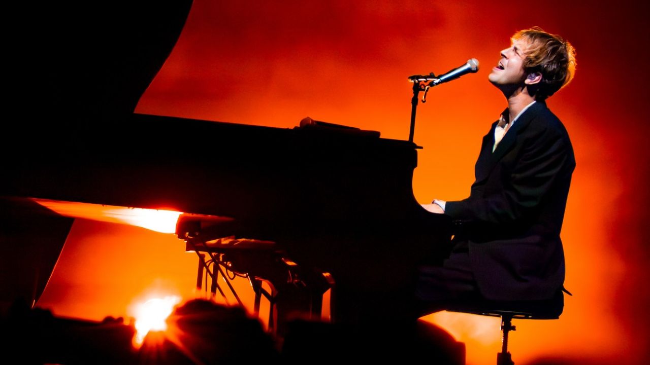 Tom Odell playing piano and singing at a concert in Dubai during a sunset.