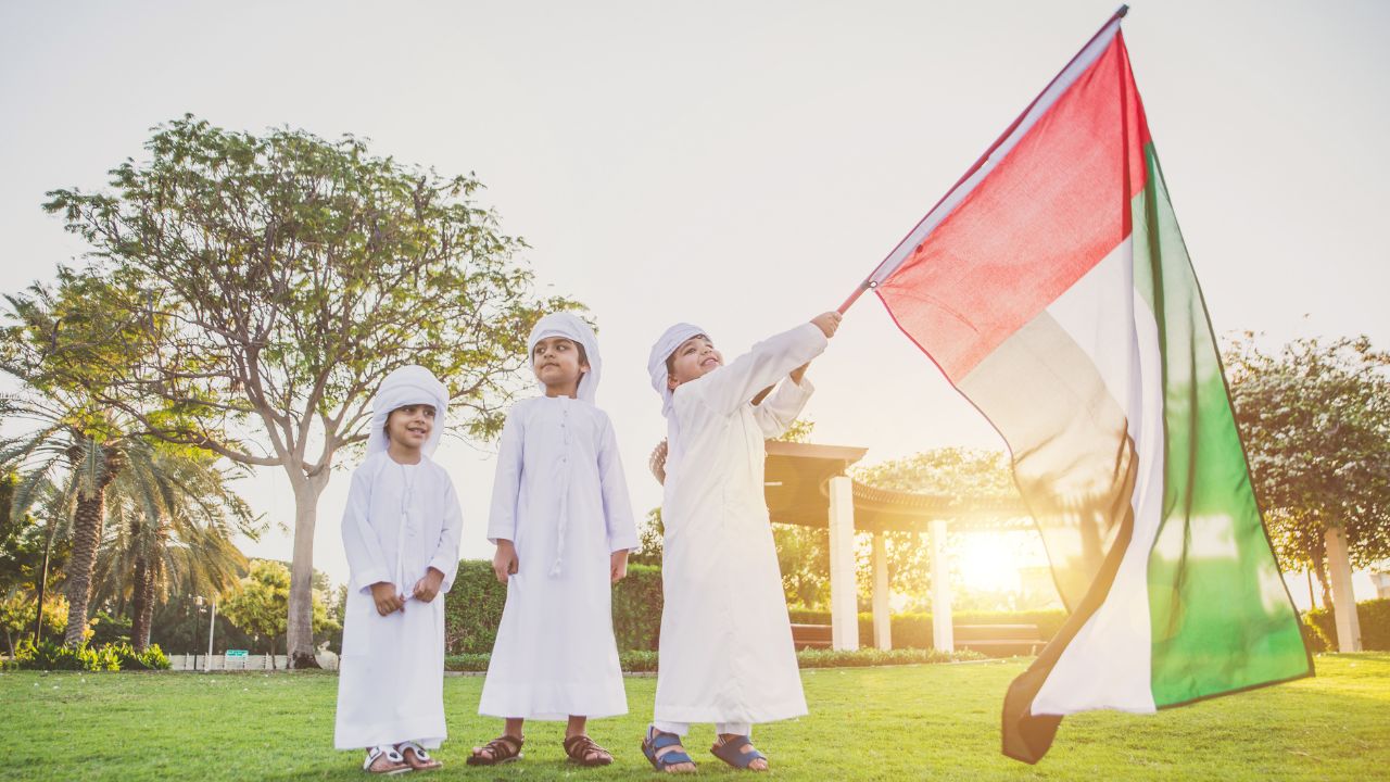 Celebrating UAE National Day outdoors Children in traditional Emirati clothing holding UAE flag during celebration.