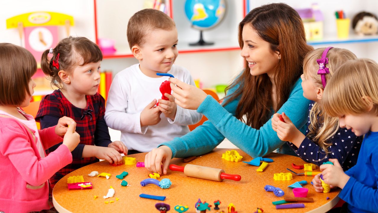 Happy teacher with children playing with toys in a colourful classroom.