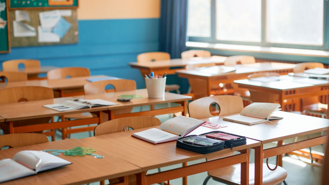School classroom with empty desks and open books, bright natural light. School classroom with empty desks, open books, and sunlight streaming through windows.