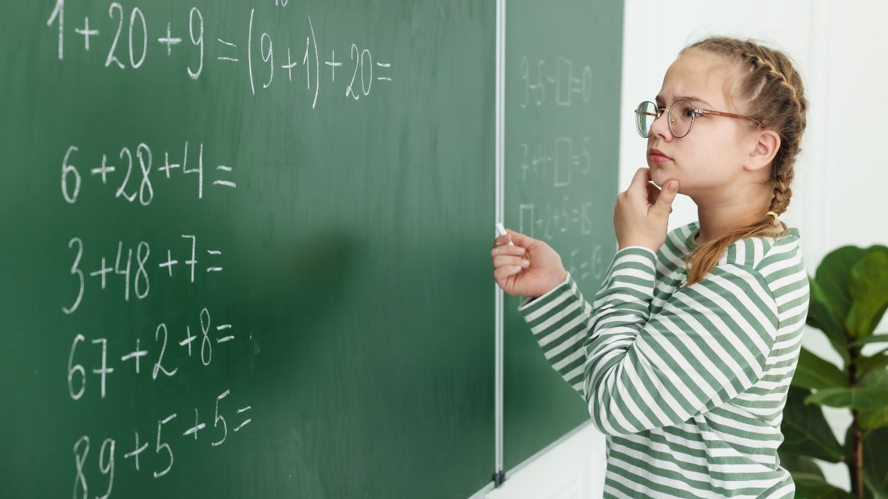 Young girl solving math problems on classroom blackboard.