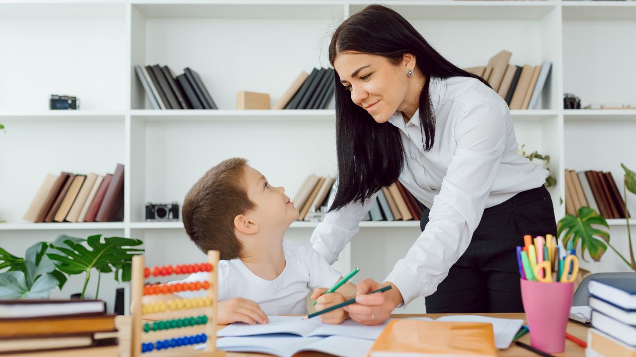 Woman helping a young boy with homework in a library setting in the UAE.
