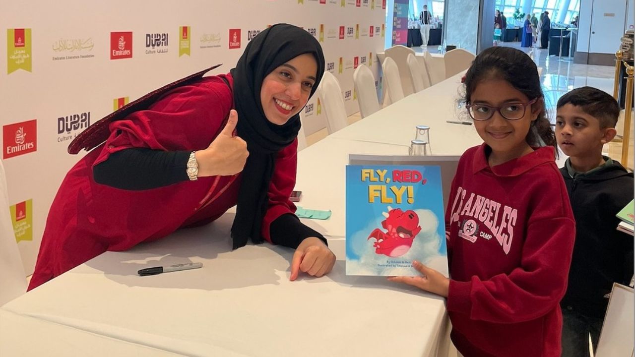 Woman and girl holding a children's book titled "Fly, Red, Fly!" at an event.