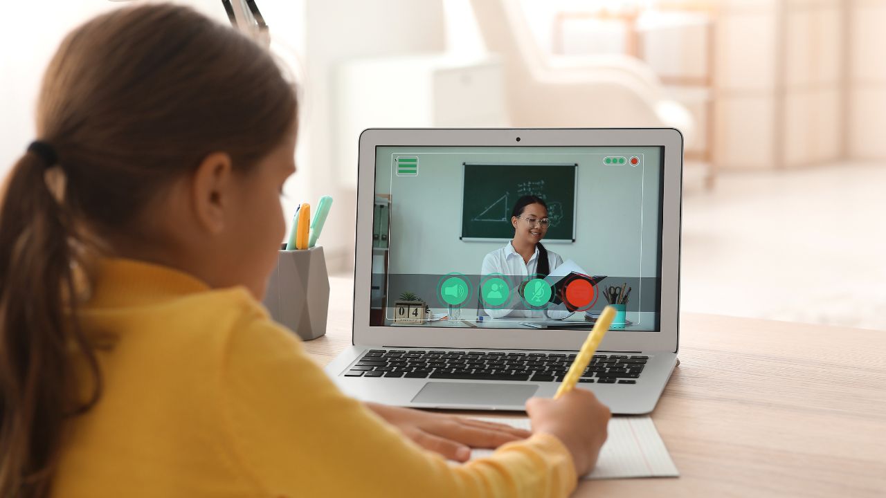 Child engaging in online learning with a teacher on a laptop.