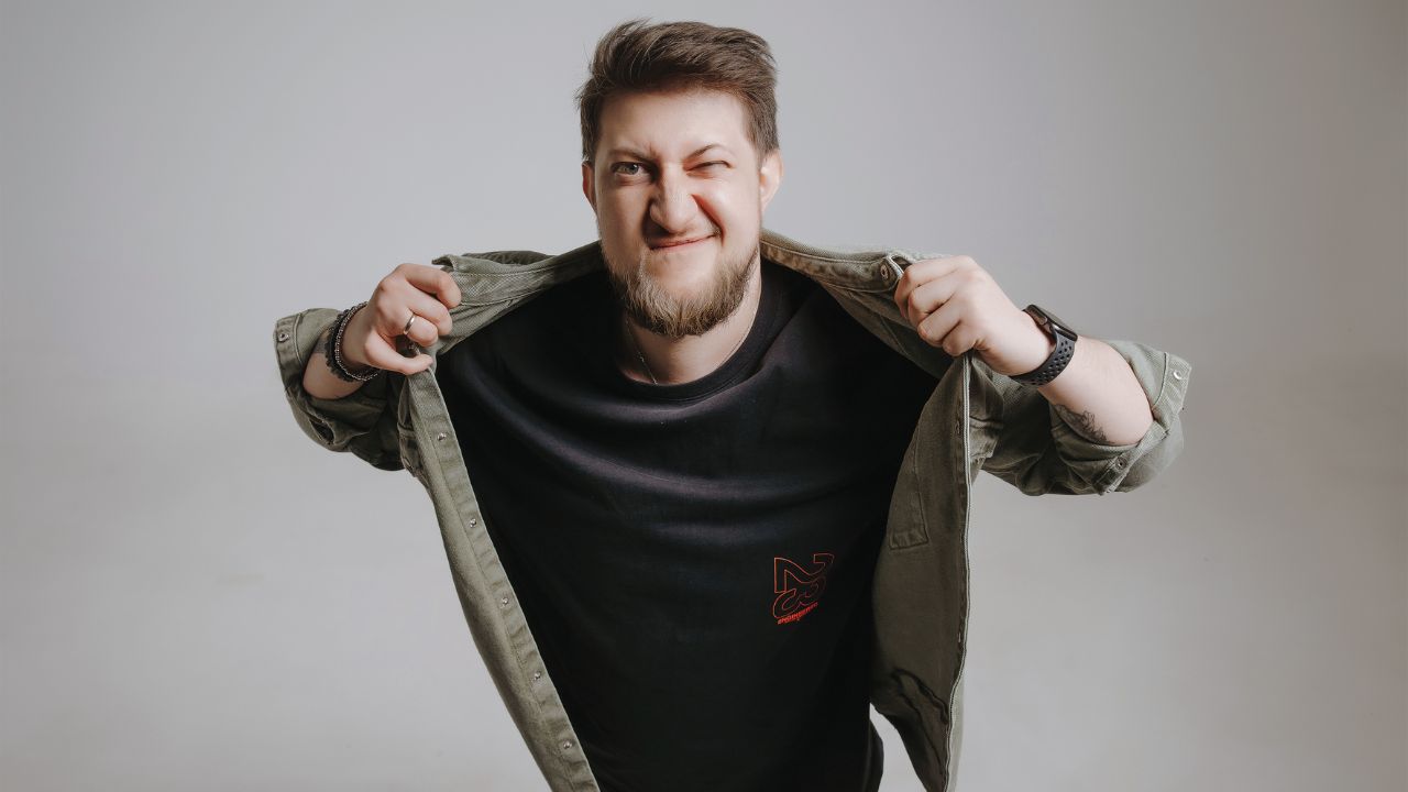 Smiling young man with beard opening jacket, casual style, neutral background.