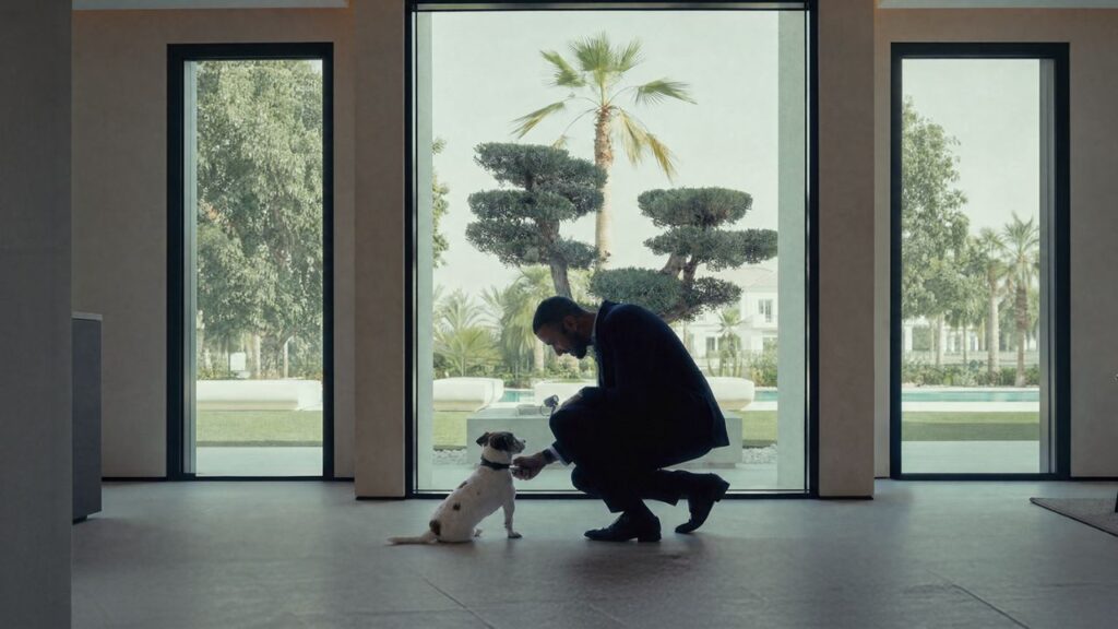Businessman kneeling with dog in sleek, modern lobby with large glass windows.