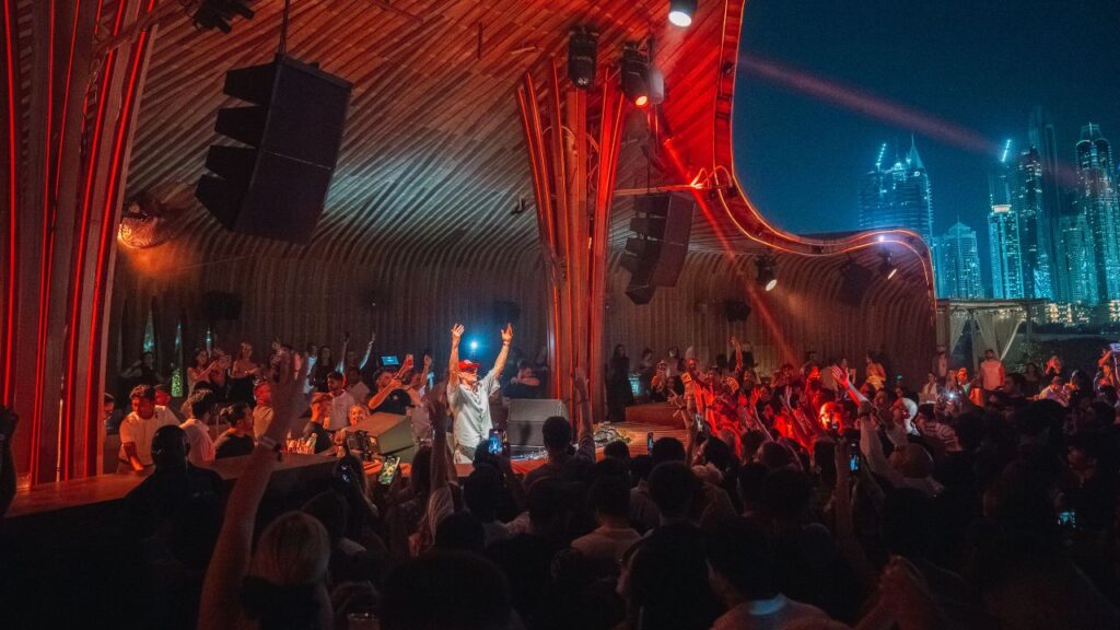 Crowd enjoying a vibrant beach party with DJ and city skyline backdrop.