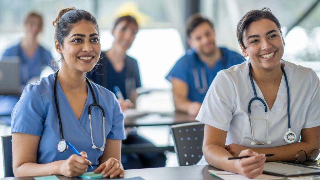 students smiling wearing nursing scrubs listening to a lecture
