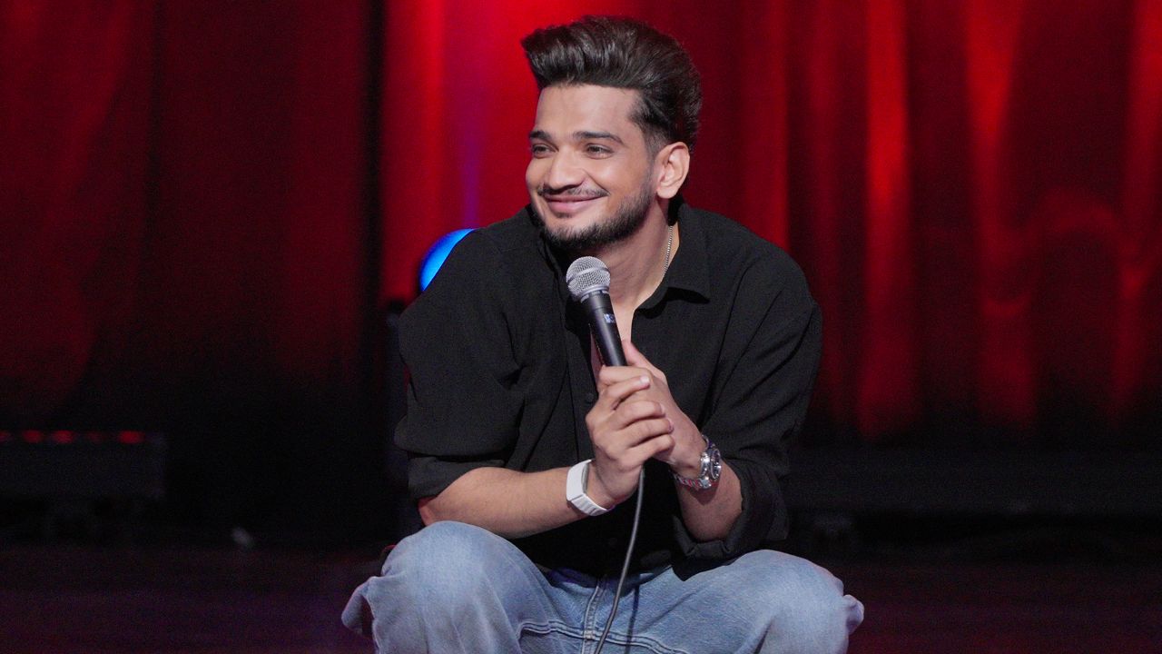 man sitting on a chair on stage holding a microphone smiling
