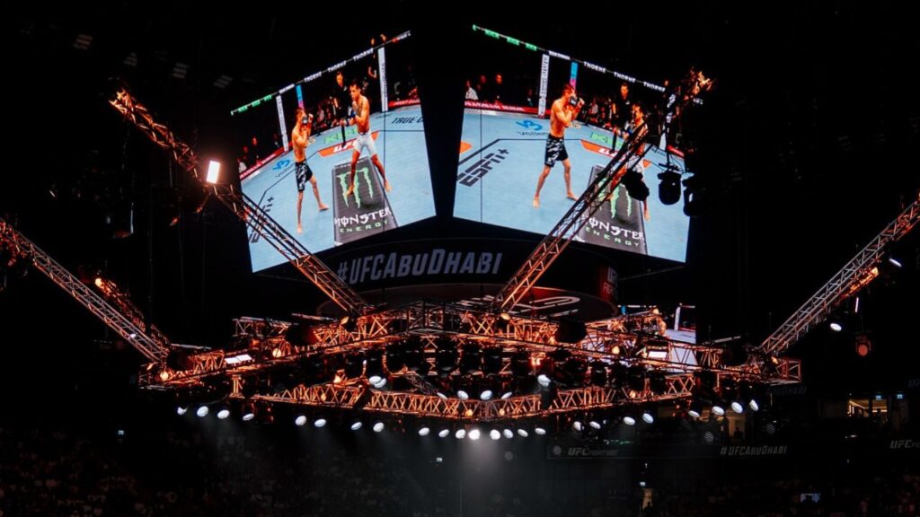 UFC Fight Night Abu Dhabi with fighters in octagon and large screens.