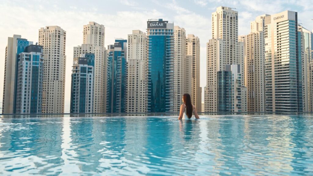 Woman relaxing in infinity pool with Dubai skyscrapers in background.