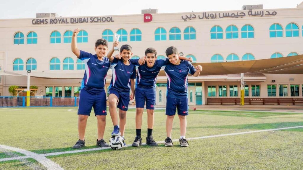 students of gems rsd wearing pe uniform in the football field posing for the camera with the logo of the school in the back