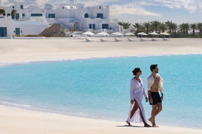 A couple strolling down the beach at Anantara Santorini Abu Dhabi