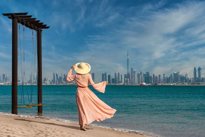 A lady with a pink dress and wind hat on beside a swing overlooking the waters and the Burj Khalifa ready for the best staycation in the UAE