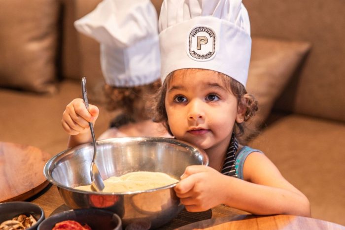 A little girl with a toque making pasta for the best indoor things to do for kids this summer