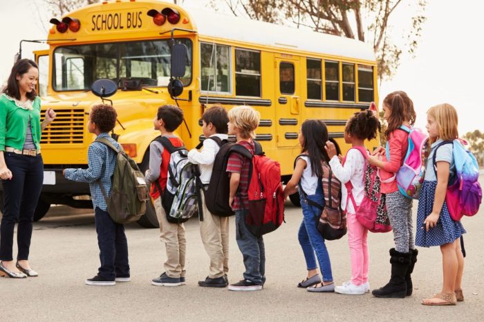 Teacher And A Group Of Elementary School Kids At A Bus Stop