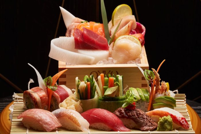 A variety of sushi, nigiri and sashimi well plated on a bamboo crate and mat. The variety includes tuna, salmon, yellowfin, wagyu nigiri, avocado roll. octopus roll, vegetable roll, California roll well garnished with microgreens, lemon and vegetables only at OKKU Dubai