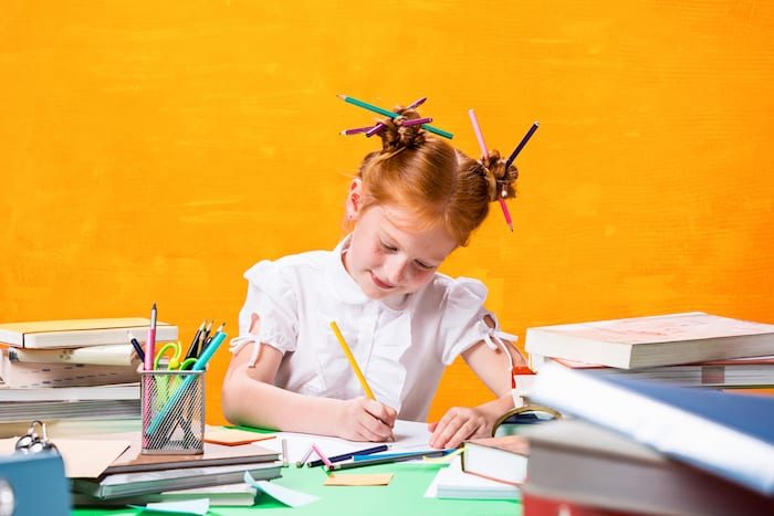 The Redhead teen girl with lot of books sitting at table on orange studio background. The education and back to school concept