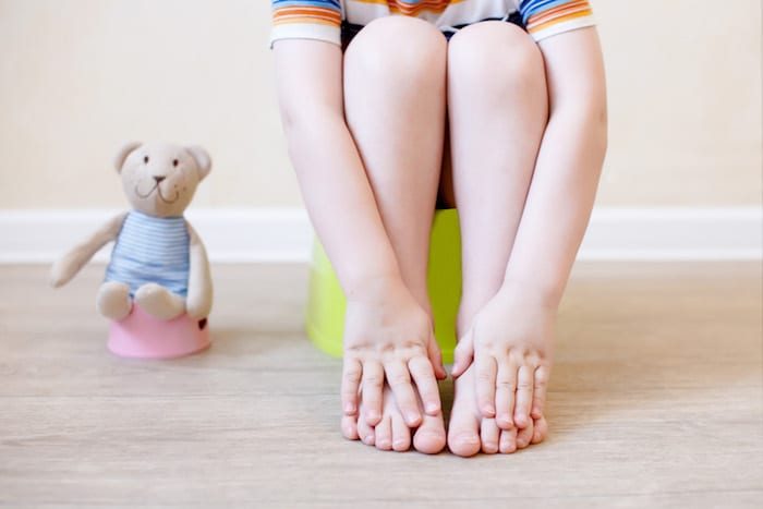 closeup of legs of the child sitting on the potty. the idea of training the child to the potty with a toy bear, which also sits on a toy potty